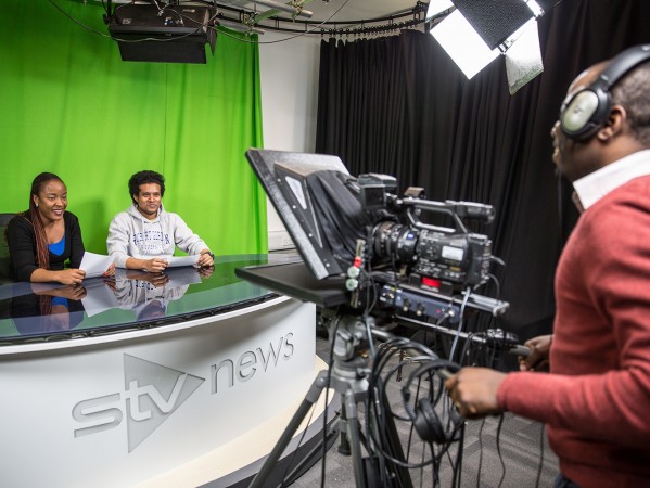 two students sitting in front of a greenscreen to be filmed for a news style report