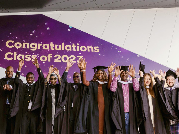 Graduates in gowns and hats with their hands in the air. Behind them is a sign saying 'Congratulations Class of 2023' Graduates in gowns and hats with their hands in the air. Behind them is a sign saying 'Congratulations Class of 2023'